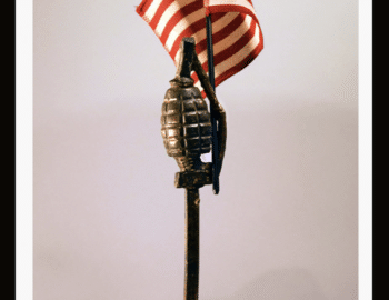 Bronze cast grenade sculpture titled "Pivotal Moment" (2016) by Elisabeth Jacobsen, featuring a U.S. flag and marble base. Dimensions: 15 x 4 x 6 inches.